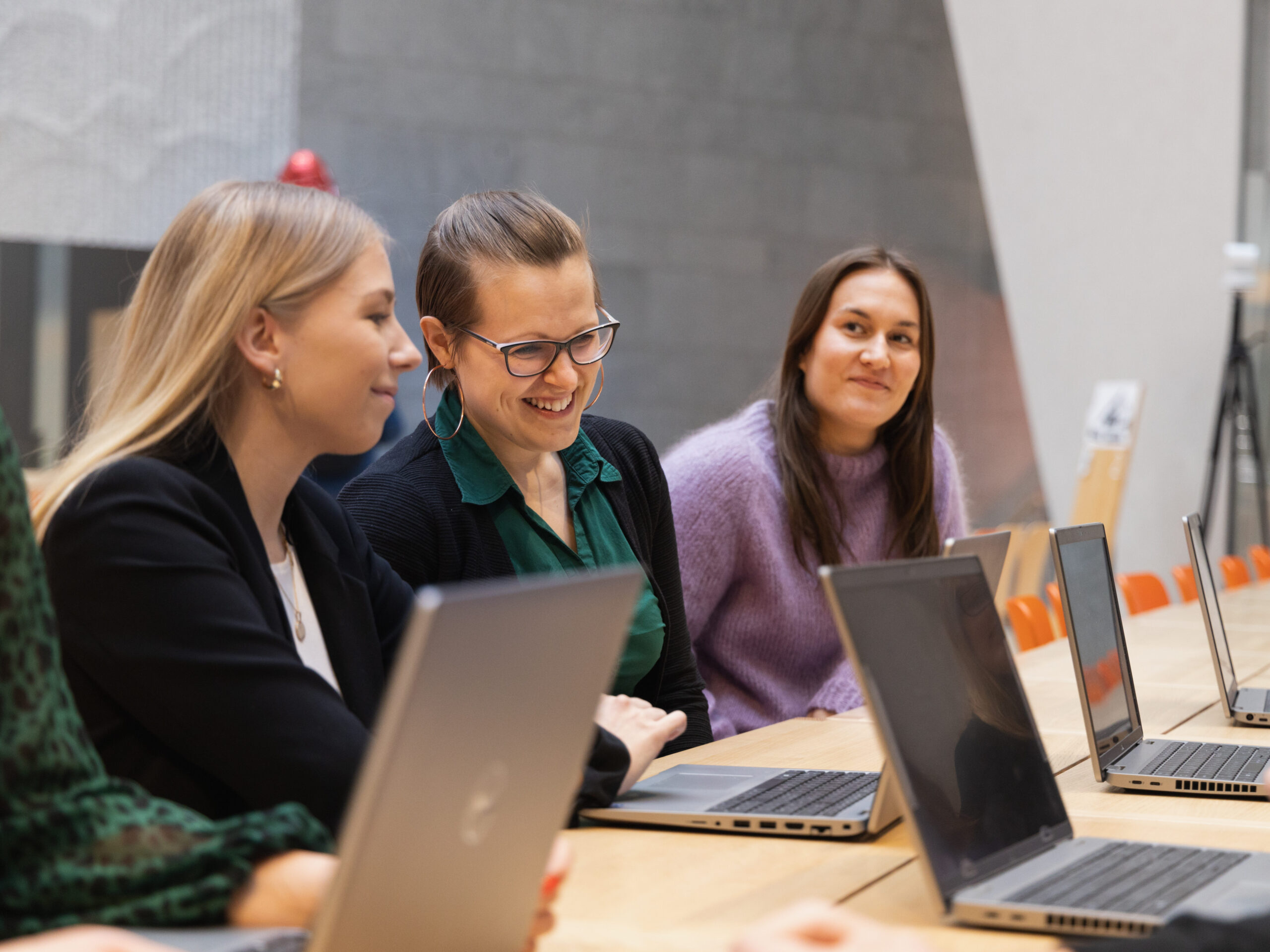 Three laughing people at a table with multiple laptops.