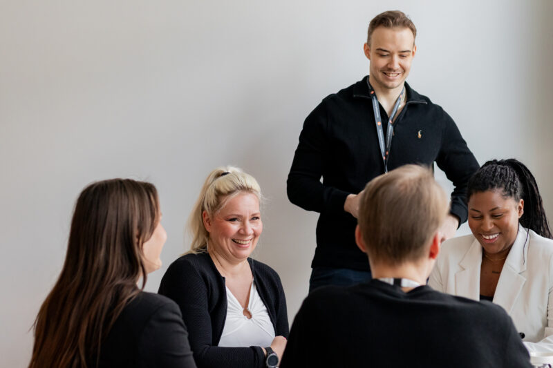 Tribedo yritystarina kuvituskuva, jossa viisi iloista ihmistä pöydän ympärillä