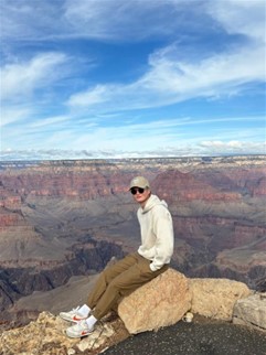 Elias istumassa kivellä. Kuva otettu kaukaa ja taustamaisemana rotkomaisema.