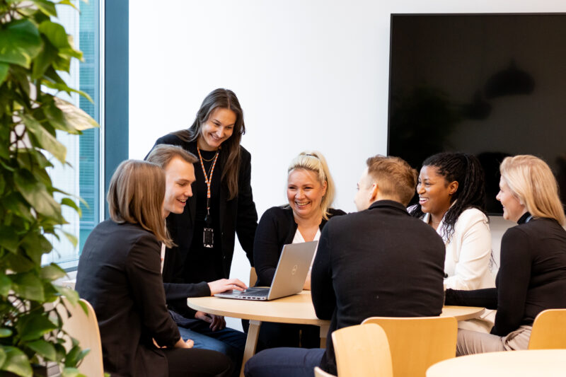 Tribedon henkilöstöä pöydän ympärillä kuvaten blogin otsikkoa Parempi työpäivä pienillä teoilla – käytännön esimerkkejä Tribedon arjesta