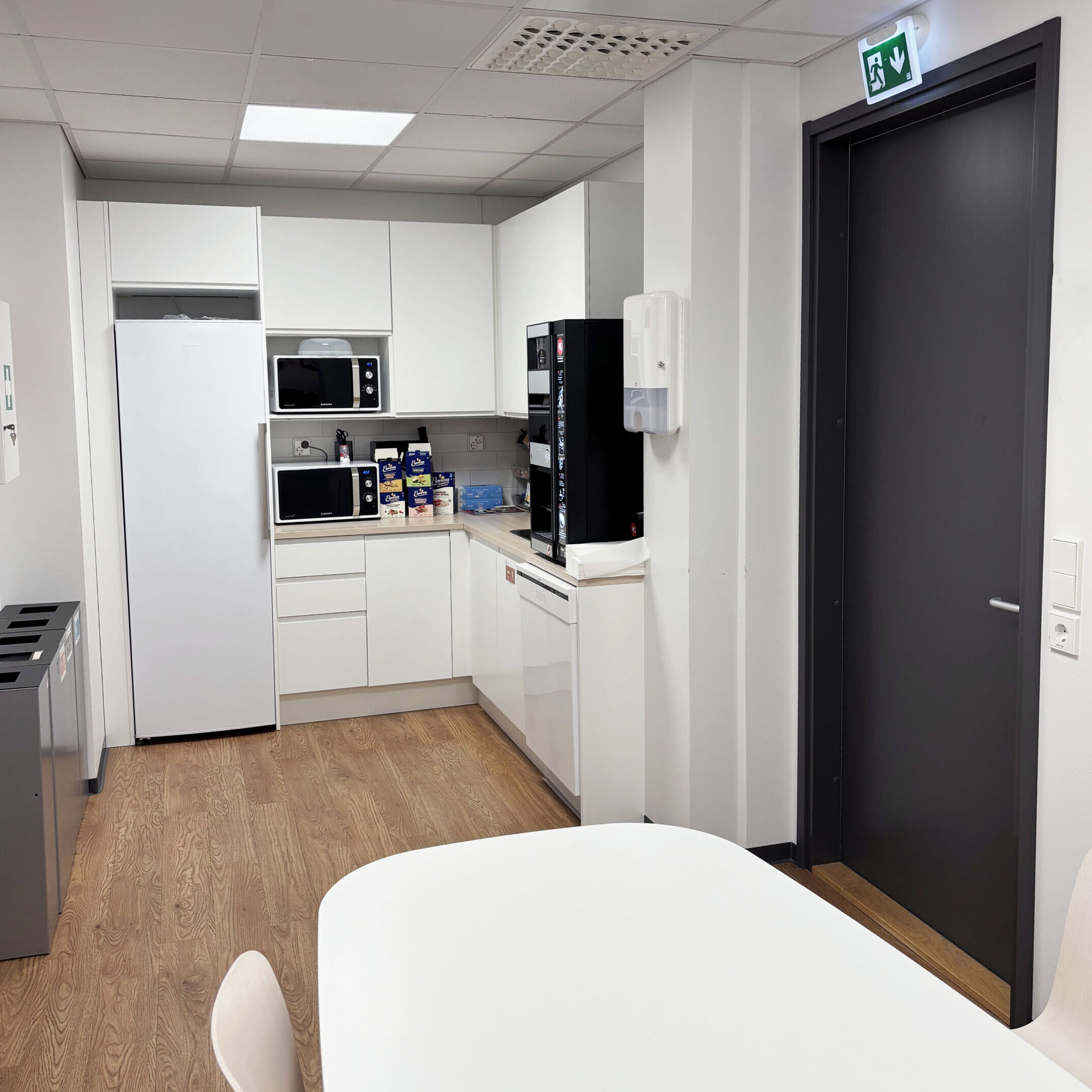 Tribedo Oulu valkoinen taukokeittiö, jossa jääkaappi, mikroaaltouuneja, kahvikone ja ruokapöytä.