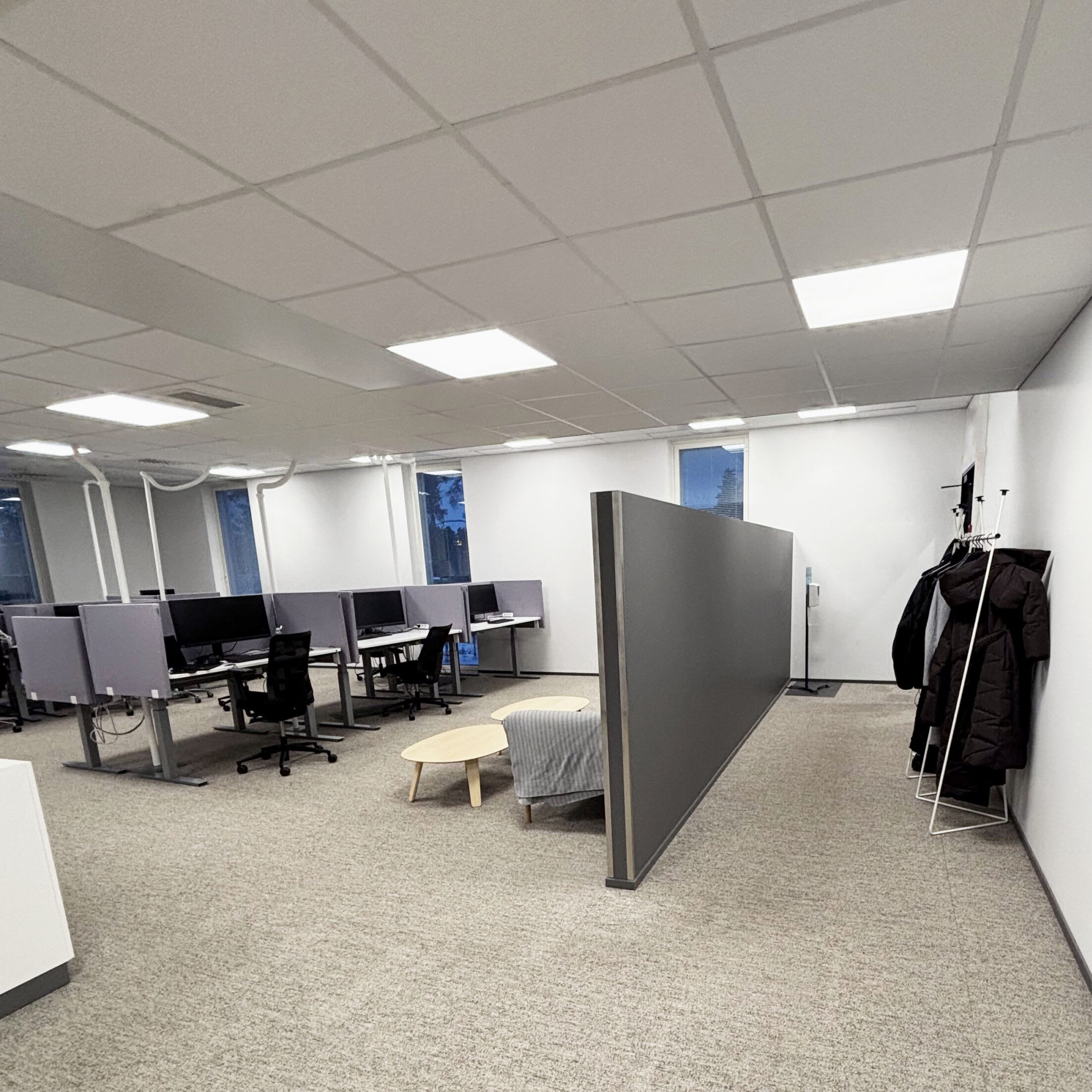 Tribedo Oulu toimistotila, jossa useita työpisteitä ja tilaa jäsentäviä sermejä sekä ripustustilaa seinustalla.