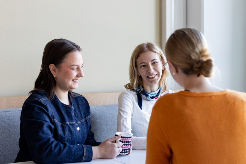 Kolme henkilöä kahvipöydän äärellä toimistoympäristössä keskustelemassa aiheesta tribevire.